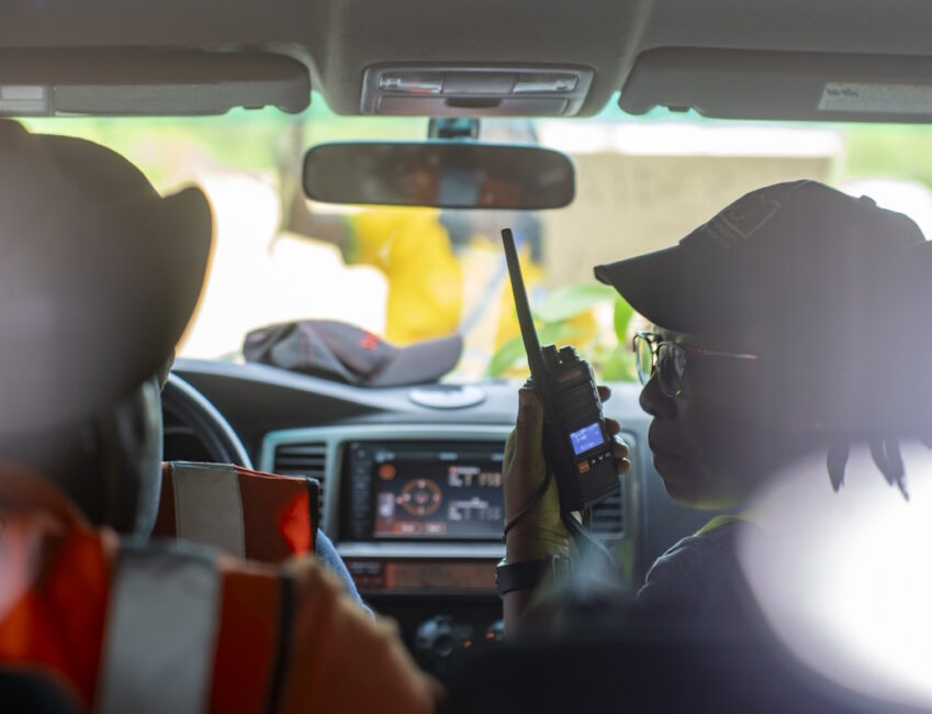 Deux professionnels en intervention de terrain dans un véhicule, utilisant une radio pour coordonner les actions en zone sensible.