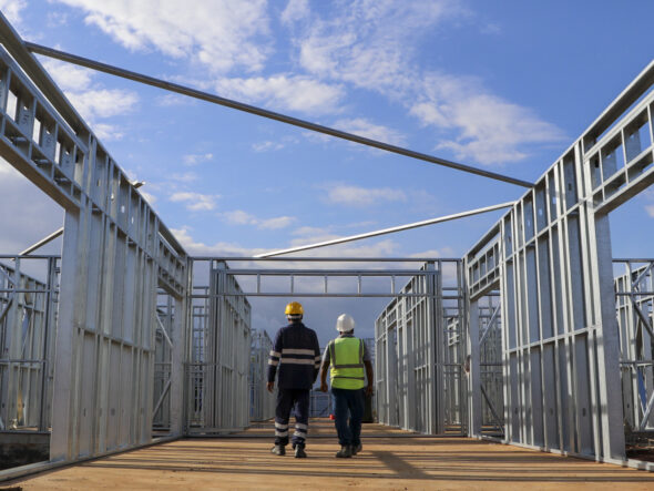 Deux travailleurs en équipements de sécurité marchent à travers une structure métallique en cours de construction, illustrant le renforcement des capacités professionnelles.